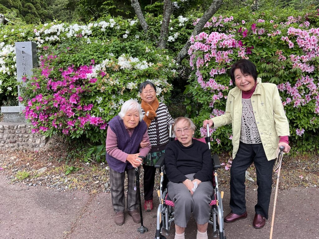 施設の入居者と職員が花壇前で記念撮影。明るい表情で季節の花を背景に。